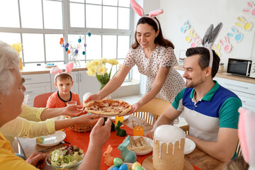 Young woman bringing pizza at Easter dinner with her family in kitchen