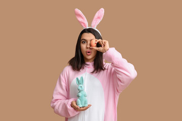 Obraz na płótnie Canvas Beautiful young woman in bunny costume with Easter egg and rabbit on brown background