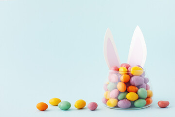 Colorful candy jar decorated with bunny ears against blue background, gifts for Easter