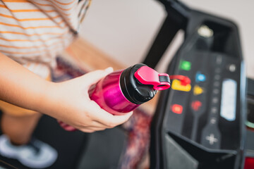 Young girl running on the treadmill with a sports water bottle in hand