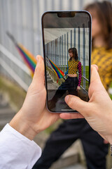 woman's hands holding a smartphone taking a photo of a young man with an umbrella in the colors of...