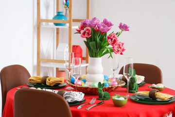 Festive Easter table setting with vase of flowers, cutlery, glasses and painted eggs