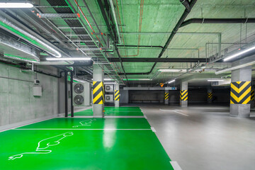 Empty underground parking lot with spaces for electric cars. Modern office building. Ecological...