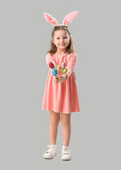 Obraz na płótnie Canvas Cute little girl in bunny ears with Easter eggs on grey background