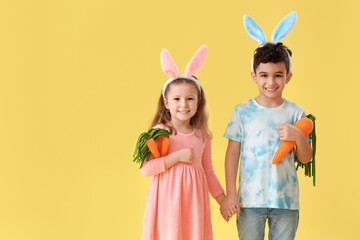 Cute little children in bunny ears with toys carrots on yellow background. Easter celebration