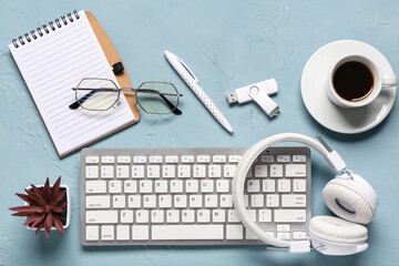 Computer keyboard, headphones, notebook and cup of coffee on blue background