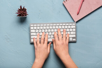 Female hands typing with computer keyboard near notebook on blue background
