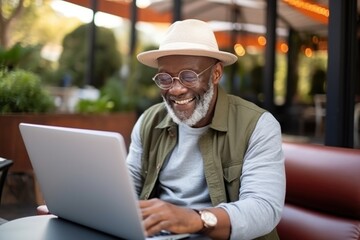 Senior African American man in casual clothes happily uses laptop to work. When he enters retirement age He still enjoys doing business. - obrazy, fototapety, plakaty
