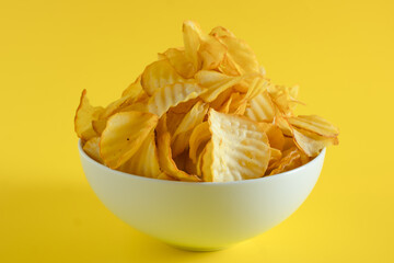 Close-up of potato chips or crisps in bowl against yellow background. perfect for recipes, articles, catalogues, or commercials 