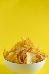 Close-up of potato chips or crisps in bowl against yellow background. perfect for recipes, articles, catalogues, or commercials 