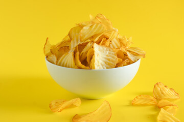 Close-up of potato chips or crisps in bowl against yellow background. perfect for recipes, articles, catalogues, or commercials 