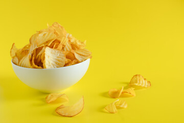 Close-up of potato chips or crisps in bowl against yellow background. perfect for recipes, articles, catalogues, or commercials 
