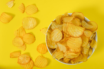 Close-up of potato chips or crisps in bowl against yellow background. perfect for recipes, articles, catalogues, or commercials 