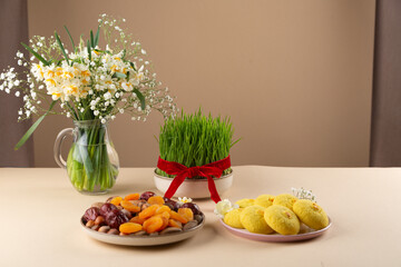 Novruz table setting with green samani wheat grass with red ribbon, dried fruits, sweet pastry, candles, kelagai and blooming flowers, spring or new year celebration in Azerbaijan, copy space