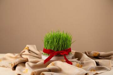 Novruz table setting with green samani wheat grass with red ribbon on traditional kelagai scarf,...
