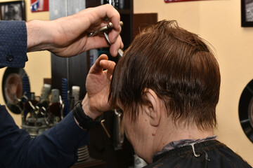 A hairdresser using a comb and scissors shortens the hair of a bang, side view.
