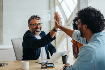 Business colleagues celebrating successful project in a creative boardroom