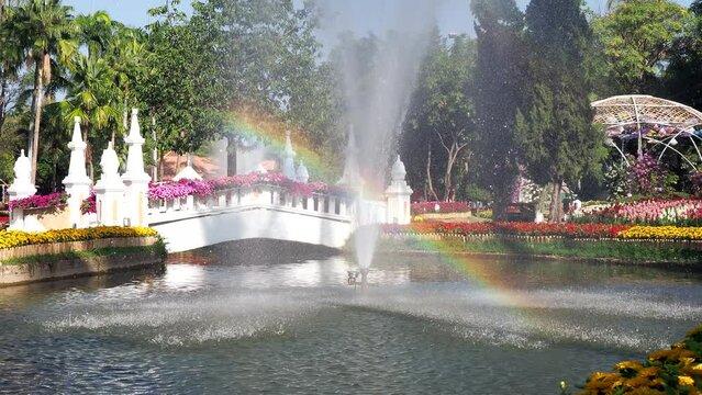 Artificial fountain with reflected bubble water rainbow in natural park under clear blue sky