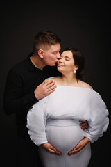 Husband kisses wife isolated on black studio background. Loving couple smiling embrace together. Pregnant woman, handsome man hugging tummy. Parenthood concept. Waiting baby. Nine months. Closeup.