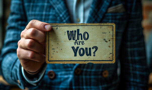Close up of a man in a suit holding a card with Who Are You? printed on it, questioning identity and self perception