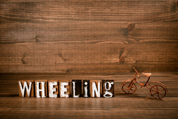 WHEELING. Text from alphabet blocks and rusty miniature bicycle on wood texture background