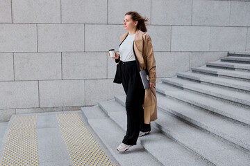 A professional businesswoman strolls confidently towards the office building, balancing her laptop...