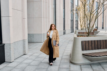 Business woman walks through the bustling city streets, exuding elegance in her his trench coat,...