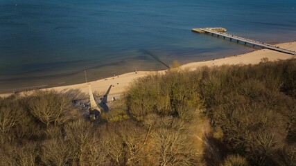 Kołobrzeg pier on a sunny February afternoon. Windless weather, calm sea without a single wave, tourists strolling on the pier. - obrazy, fototapety, plakaty
