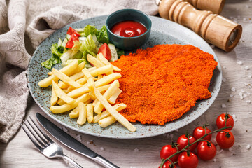 schnitzel, french fries with tomato sauce and salad on a wooden background.