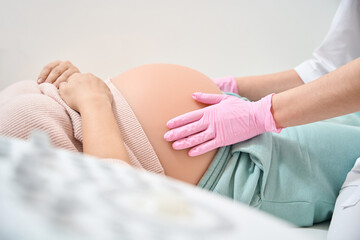 Gynecologist-obstetrician in medical gloves examining belly of pregnant woman