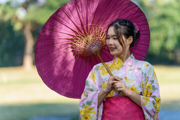 A young woman wearing a Japanese traditional kimono or yukata holding an umbrella is happy and cheerful in the park.