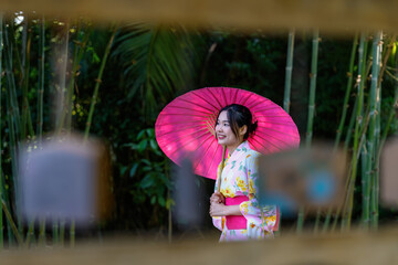 A young woman wearing a Japanese traditional kimono or yukata holding an umbrella is happy and...