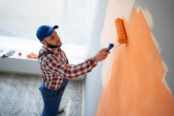 Painter paints a wall orange with a paint roller, top view