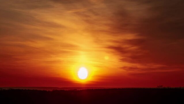 Amazing sunset in orange sky with dark dramatic clouds, Timelapse. 4K. Bright sun setting down above the horizon. Colorful sunset, epic clouds. Vibrant color. Time-lapse. Sundown, cloudscape