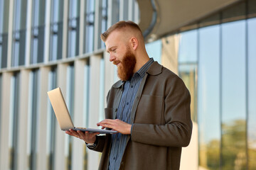 Fototapeta premium A 35-year-old man with a red beard checks mail from a laptop in his hands while walking down the street
