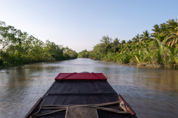 Boat peacefully traveling down a side arm of the Ham Luong River in Vietnam's Mekong Delta, through a unique landscape dominated by water, islands and tropical rainforest