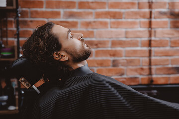 Portrait Man in barber chair. Barbershop hairdresser, brick background, warm toning