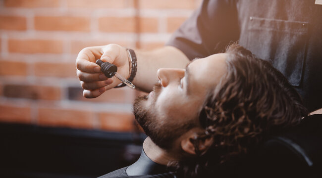 Barber use dropper with oil for beard of man in barbarshop. Concept spa care for men hair