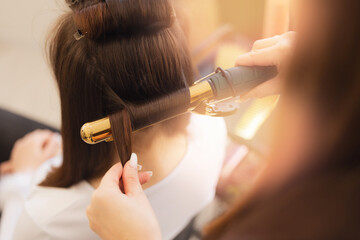 Modern hairstyle for wedding, Stylist skillfully curling hair with golden iron in salon.