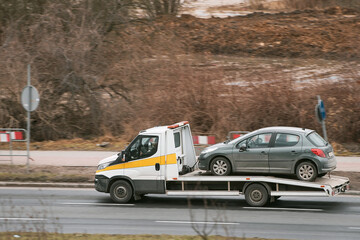 a towtruck is carrying a car that has broken down. The car has a problem with its engine and cannot...