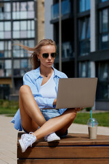 Young pretty blond woman with sunglasses solves business problems using a laptop on the street