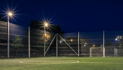 An amateur soccer field with ball illuminated at night. A small