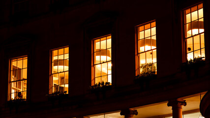 A captivating snapshot of city windows aglow with the warmth of artificial light, painting the...