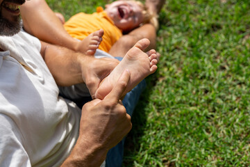 family and love concept - young father tickling his little son in park. close-up of a child's heel...