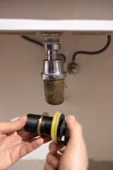 Plumber's hand holds joints and joints of sink or sink in bathroom, Cleaning clogged sink in bathroom to unclog sink.