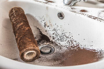 Falling dirty particles from a water filter in a white washbasin. Elements of a filtration system...