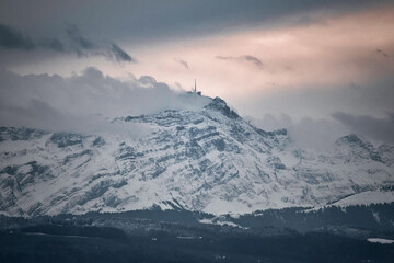 Berg mit felsen und schnee. Bergstation in Wolken gehüllt. Im Tal kein schnee und Wald.