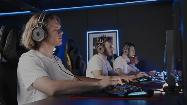 Gamers team plays a video game on PC at computer club, cyber sport tournament. E-sport championship. Five teens in headset, left-handed player. Multiplayer online battle, first-person shooter