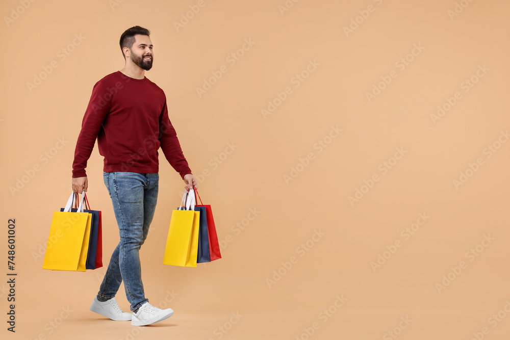 Sticker Smiling man with many paper shopping bags on beige background. Space for text