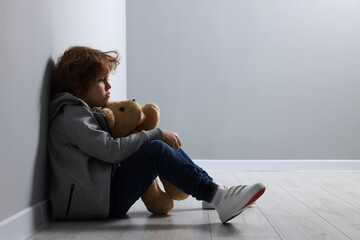 Child abuse. Upset boy with toy sitting on floor near grey wall, space for text